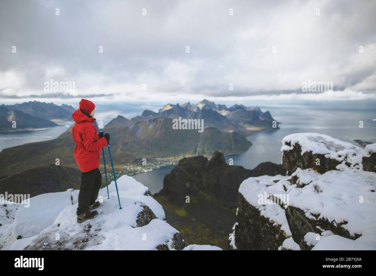 Giovane donna in giacca rossa con bastoni da trekking sulla neve montagna Foto Stock