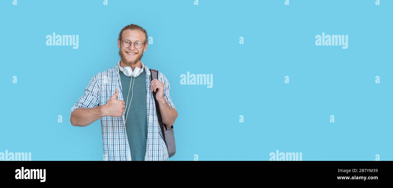Uomo sorridente studente tenere zaino pollici guardare la fotocamera isolato su blu. Foto Stock