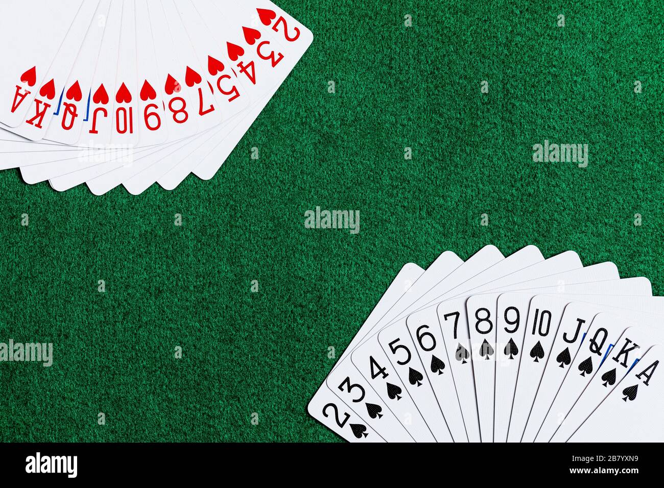 Un mazzo di carte da gioco standard con cuori e picche si è sparso negli angoli della cornice su una superficie di gioco verde feltro. Molto spazio per le copie Foto Stock