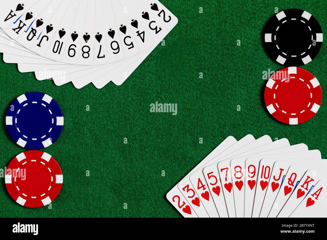 Un mazzo di carte da gioco standard con cuori e picche sparse negli angoli della cornice con chip di scommessa rosso, blu e nero nel contrario Foto Stock