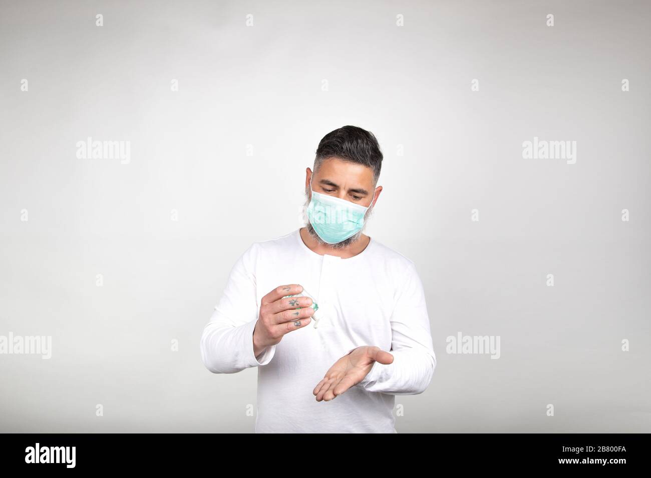 L'uomo con maschera chirurgica utilizza un disinfettante per pulire le mani dai germi su sfondo bianco. Concetto di prevenzione del coronavirus. Epidemia Foto Stock