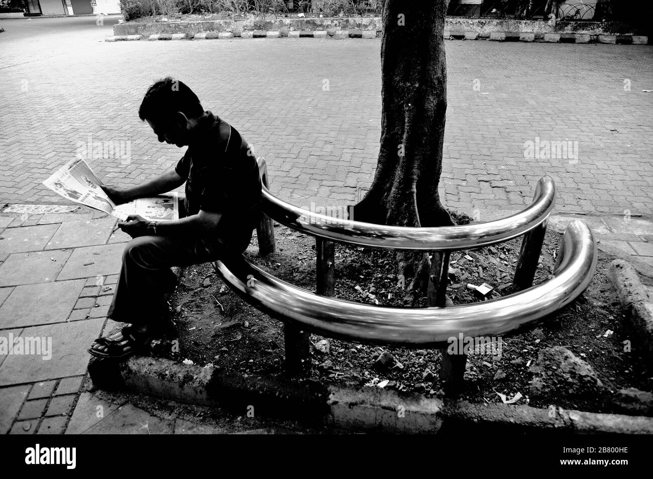 Uomo che legge giornale seduto su metallo acciaio inossidabile tubo panca, Art Plaza, Kala Ghoda, Fort, Bombay, Mumbai, Maharashtra, India, Asia Foto Stock