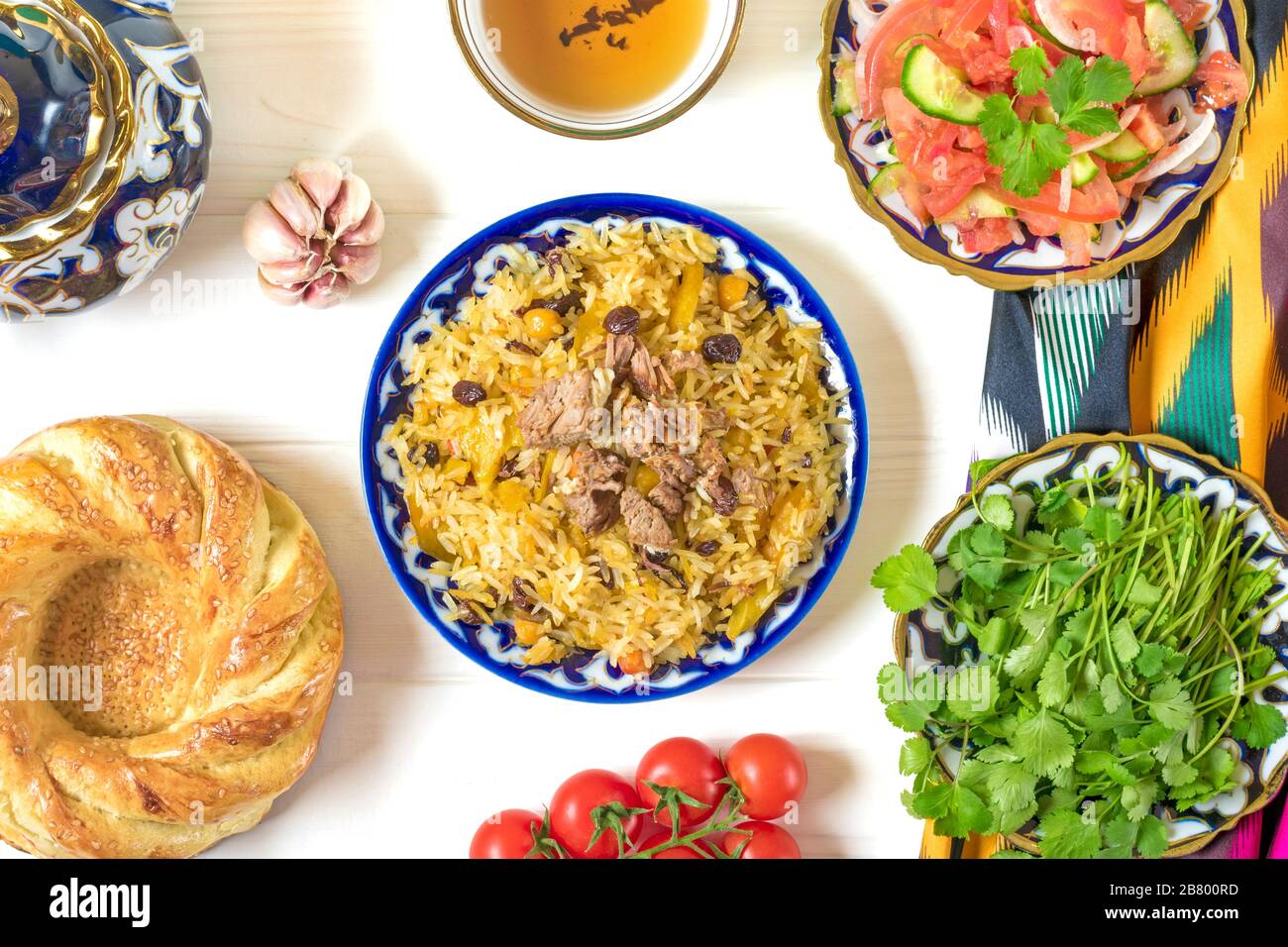 Pilaf nazionale uzbeko con carne, insalata di achichuk di pomodoro, cetriolo, cipolla in piatto con modello tradizionale, coriandolo, pomodori ciliegini, aglio, pane Foto Stock