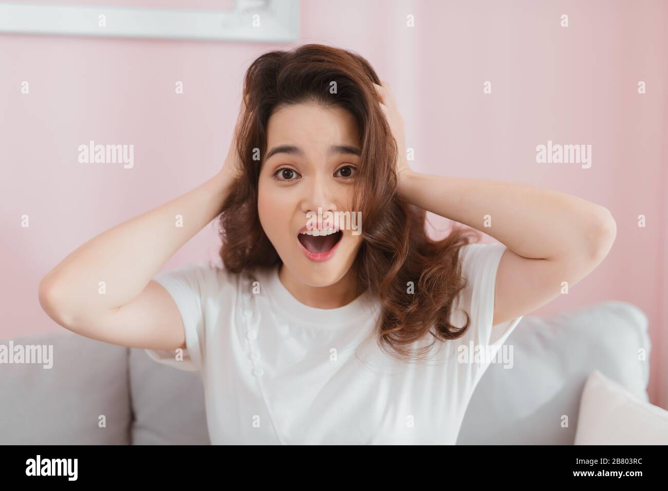 WOW. Giovane donna con capelli lunghi che guarda eccitato tenendo la bocca aperta, mani sulla testa. Scioccato sorpreso stordito. Emozione umana positiva Foto Stock