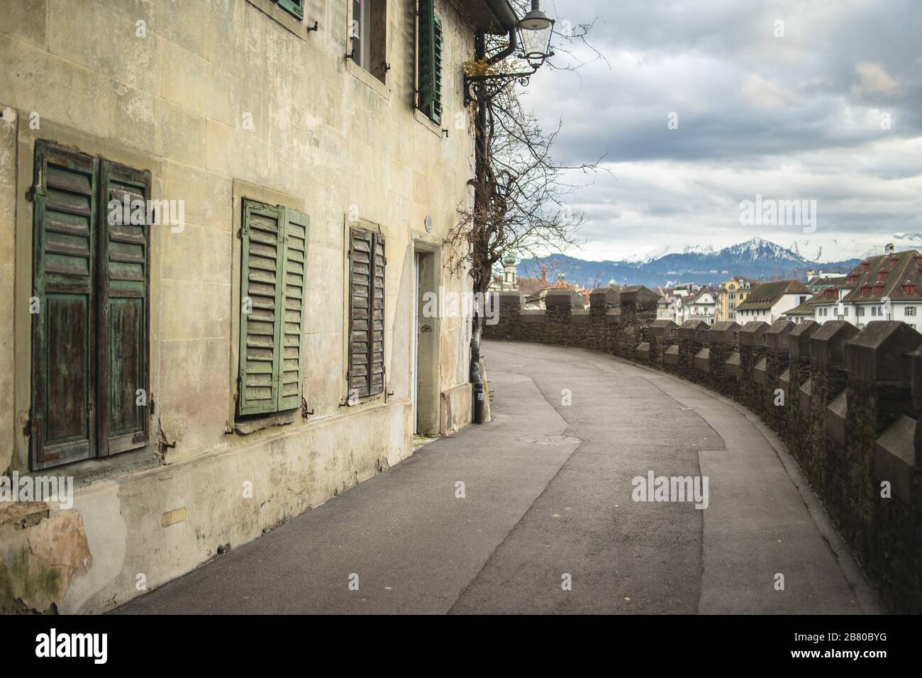 Strada posteriore curva accanto ad un vecchio edificio con persiane e la vite legnosa strisciante Foto Stock