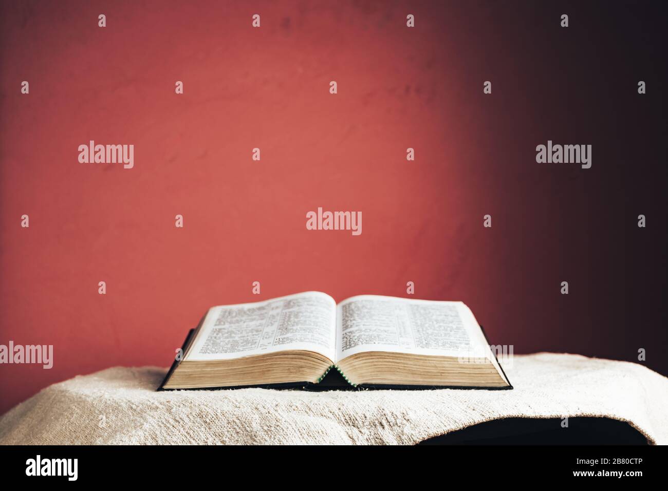 Aprire la Sacra Bibbia su un tavolo. Bellissimo sfondo rosso parete. Foto Stock