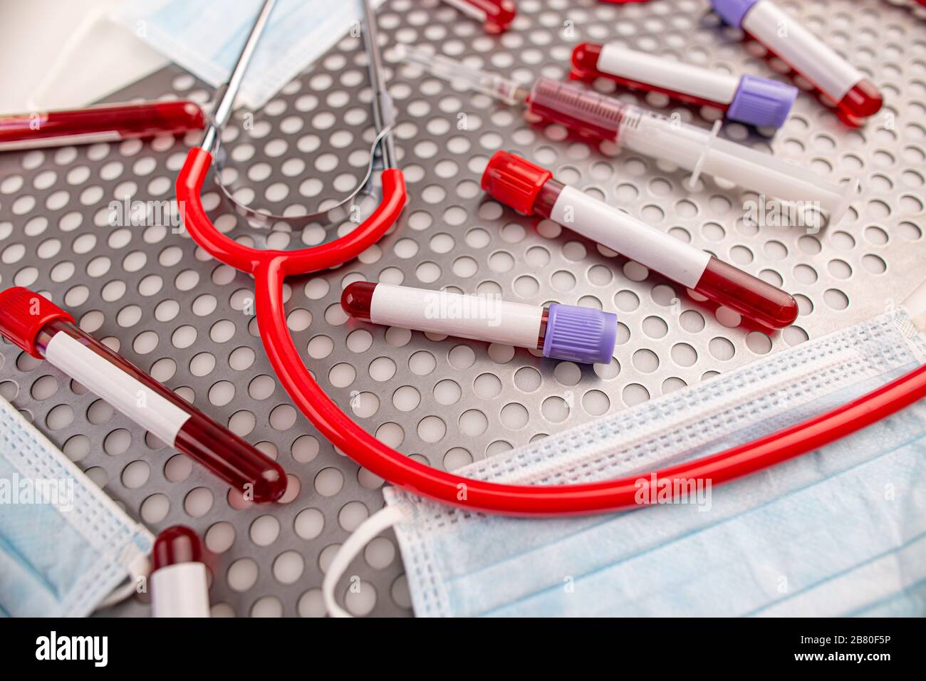 Campione di sangue in provetta con adesivo bianco vuoto per testo, siringa, maschera protettiva e stetoscopio su superficie metallica Foto Stock