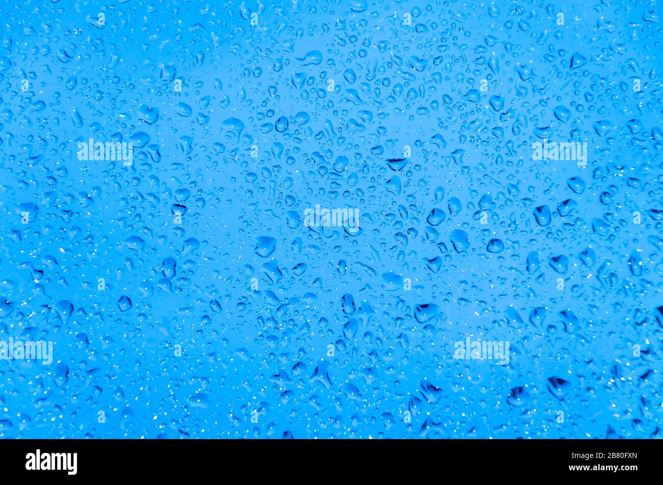 La pioggia cade sulla superficie del vetro con luce fredda blu Foto Stock