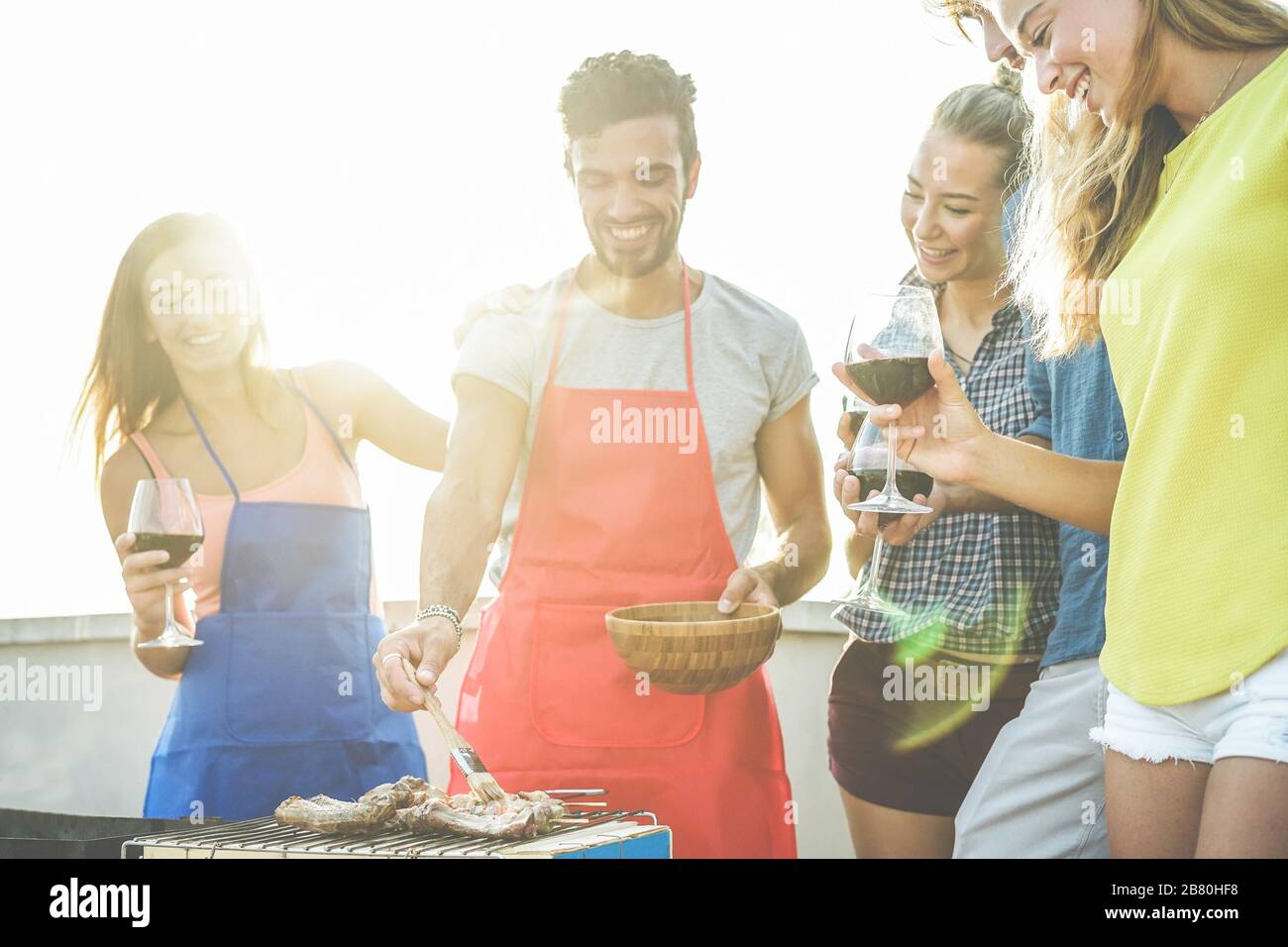 Felice studenti che cucinano e bevono vino al barbecue sul tetto cena - migliori amici grigliare carne con salsa barbecue - gioventù, cibo, amicizia concetto - Fo Foto Stock