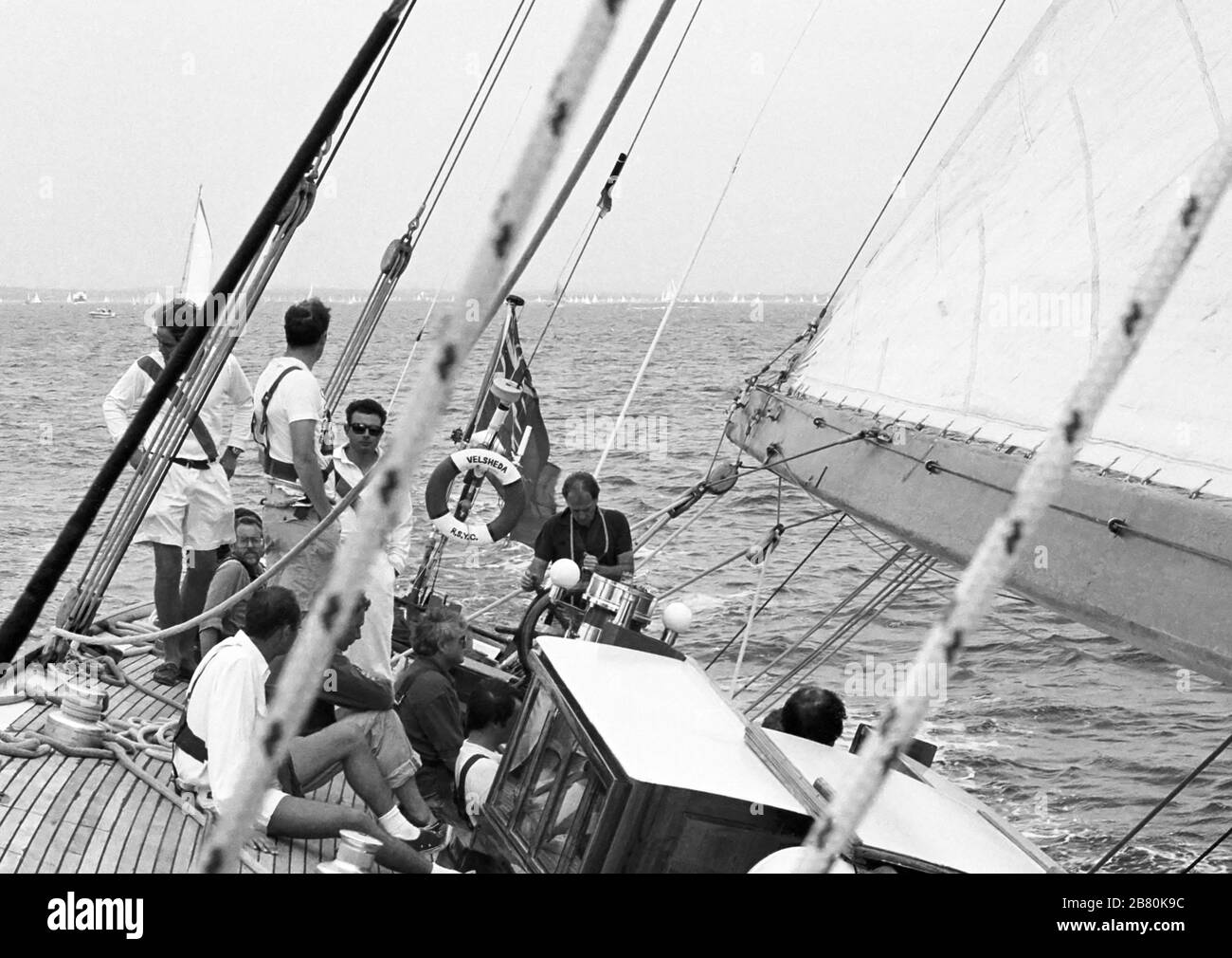 Equipaggio e afterguard a bordo di uno yacht di classe J 'Velsheda' dopo la prima rimpiazzo, navigando nel Solent, Hampshire, Inghilterra, Regno Unito, estate 1991. Archivia la fotografia di film in bianco e nero Foto Stock