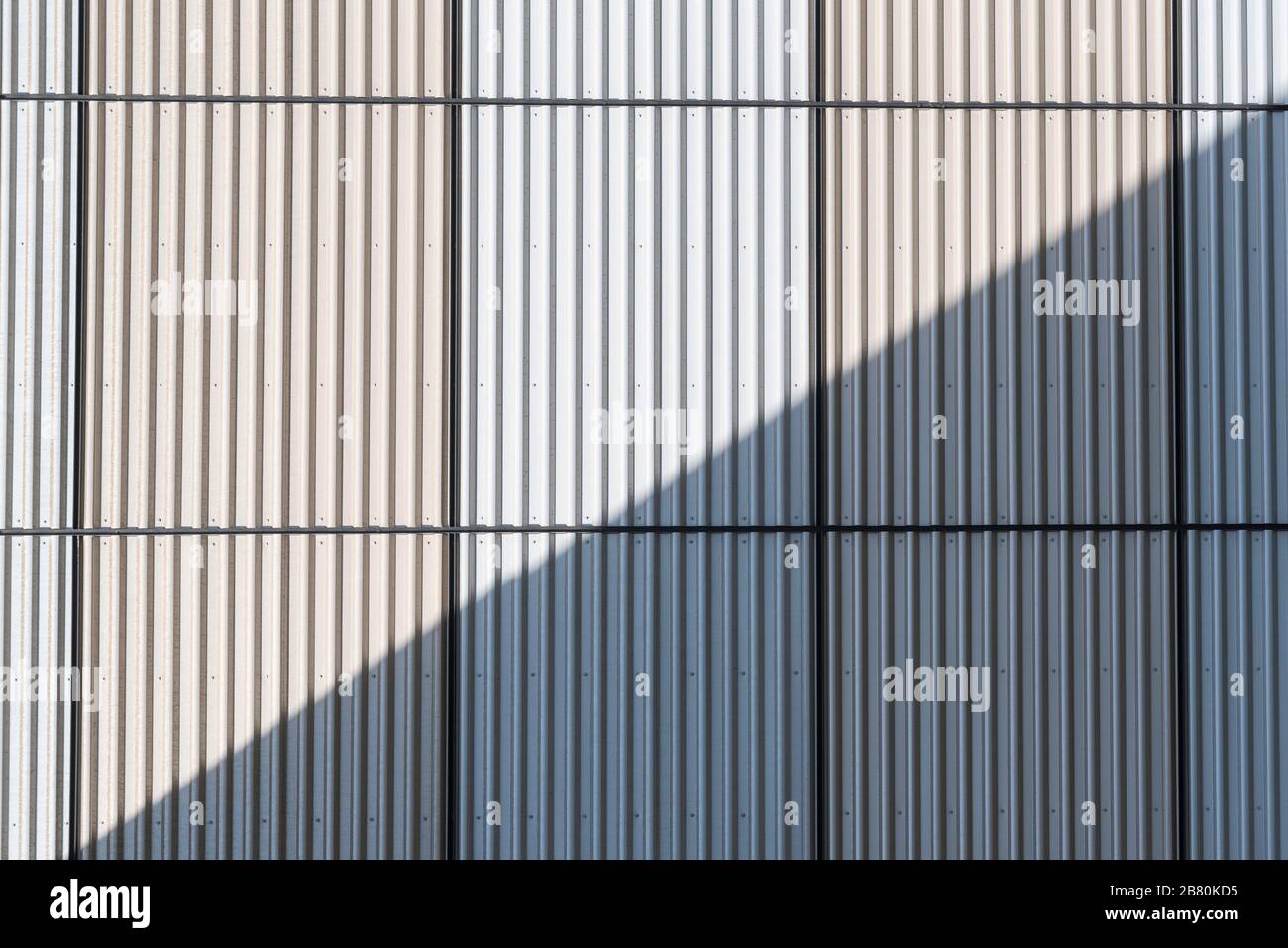 Una parete di cemento di un edificio con strisce verticali strette è sezionato diagonalmente da un'ombra da un'altra parete Foto Stock