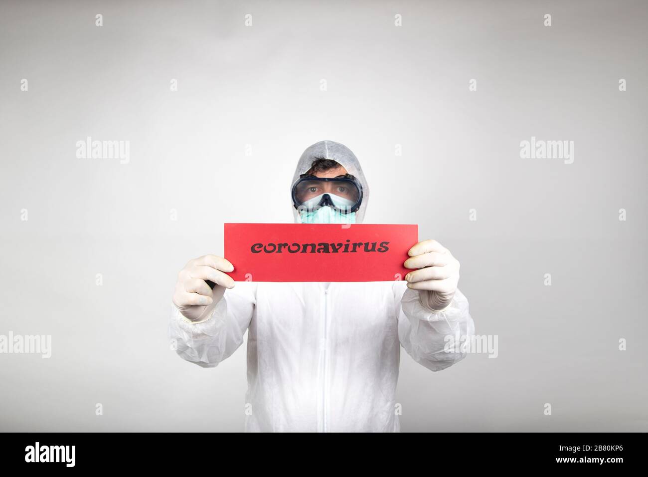 Uomo con maschera chirurgica, occhiali, tuta protettiva bianca e cartellino rosso isolato in studio su sfondo bianco. Nuova epidemia pandemica nuovo fast-spreadin Foto Stock