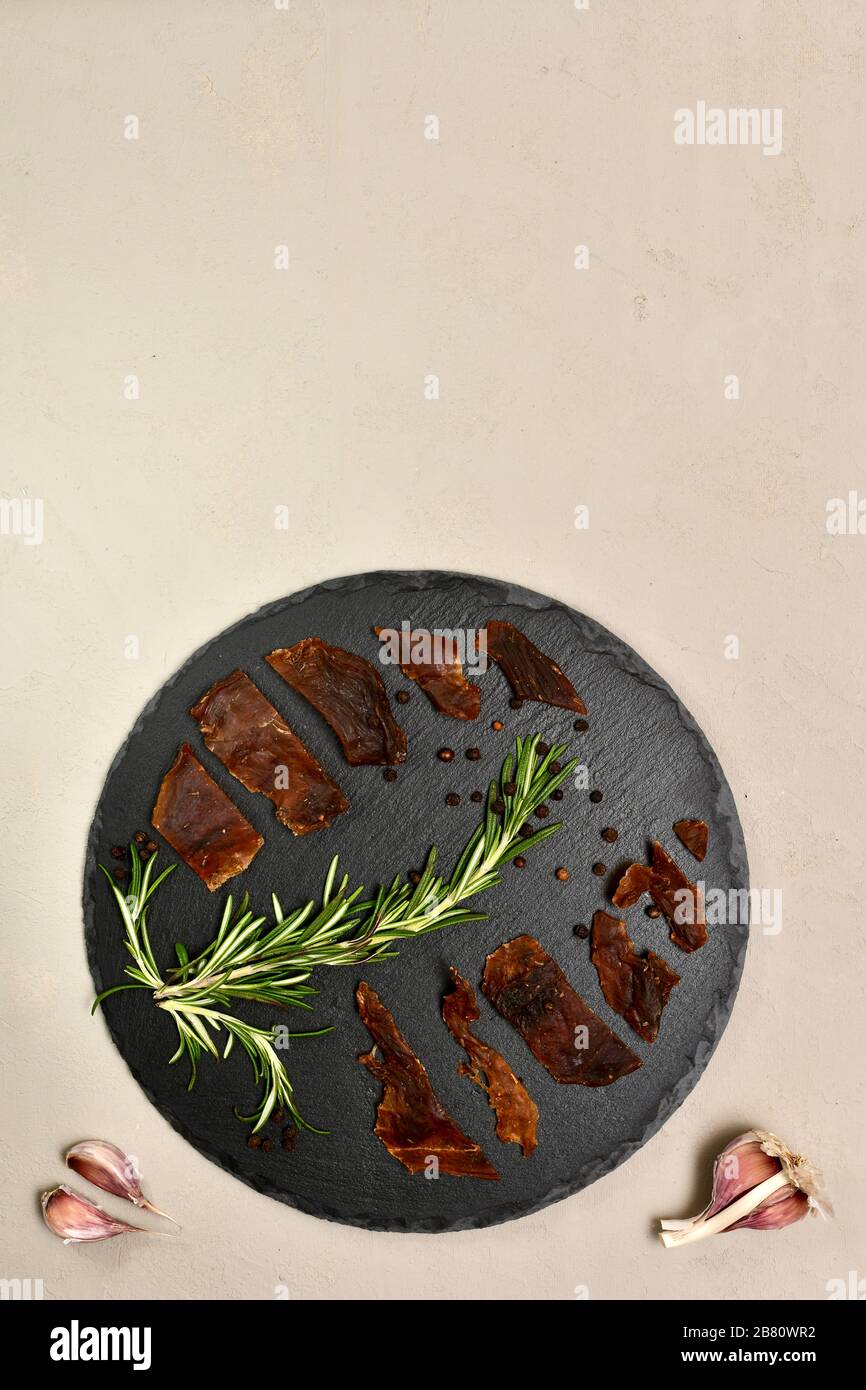 Pezzi di carne di coniglio sono disposti su un nero rotondo con pepe di aglio rosmarino su un gesso verticalmente sul fondo. Foto Stock