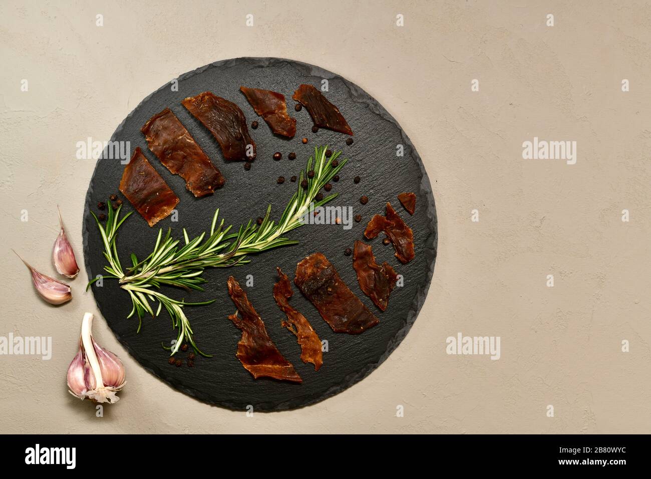 La carne di coniglio viene posata su un tondo con pepe di rosmarino con una testa di aglio strippata in un angolo a sinistra. Foto Stock