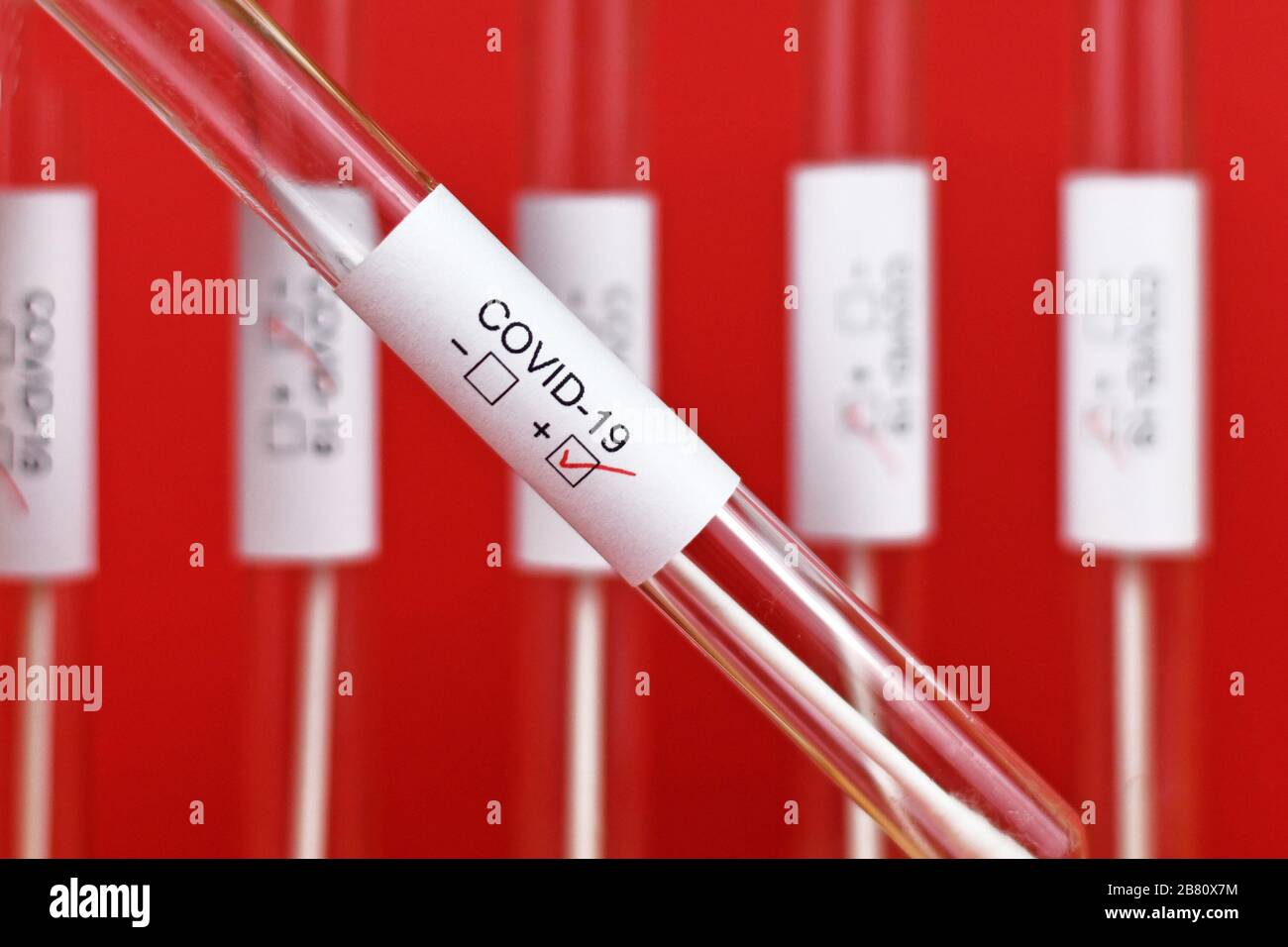 Campione di provetta per analisi medica positiva per Coronavirus con etichetta Covid-19 con altre provette blury su sfondo rosso Foto Stock