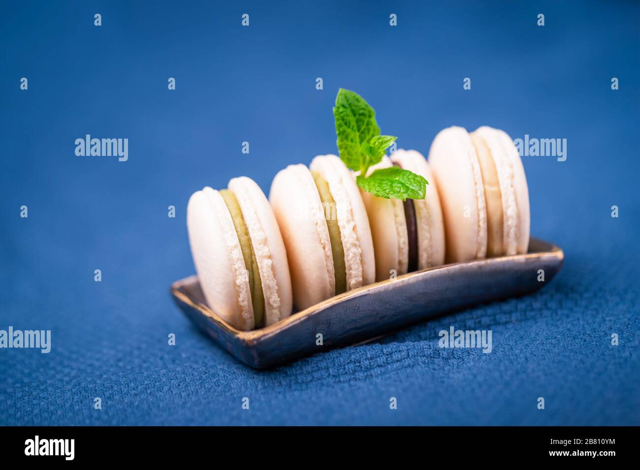 Macaroni alla vaniglia fatti in casa o macaron con foglia di menta su un classico sfondo blu Foto Stock