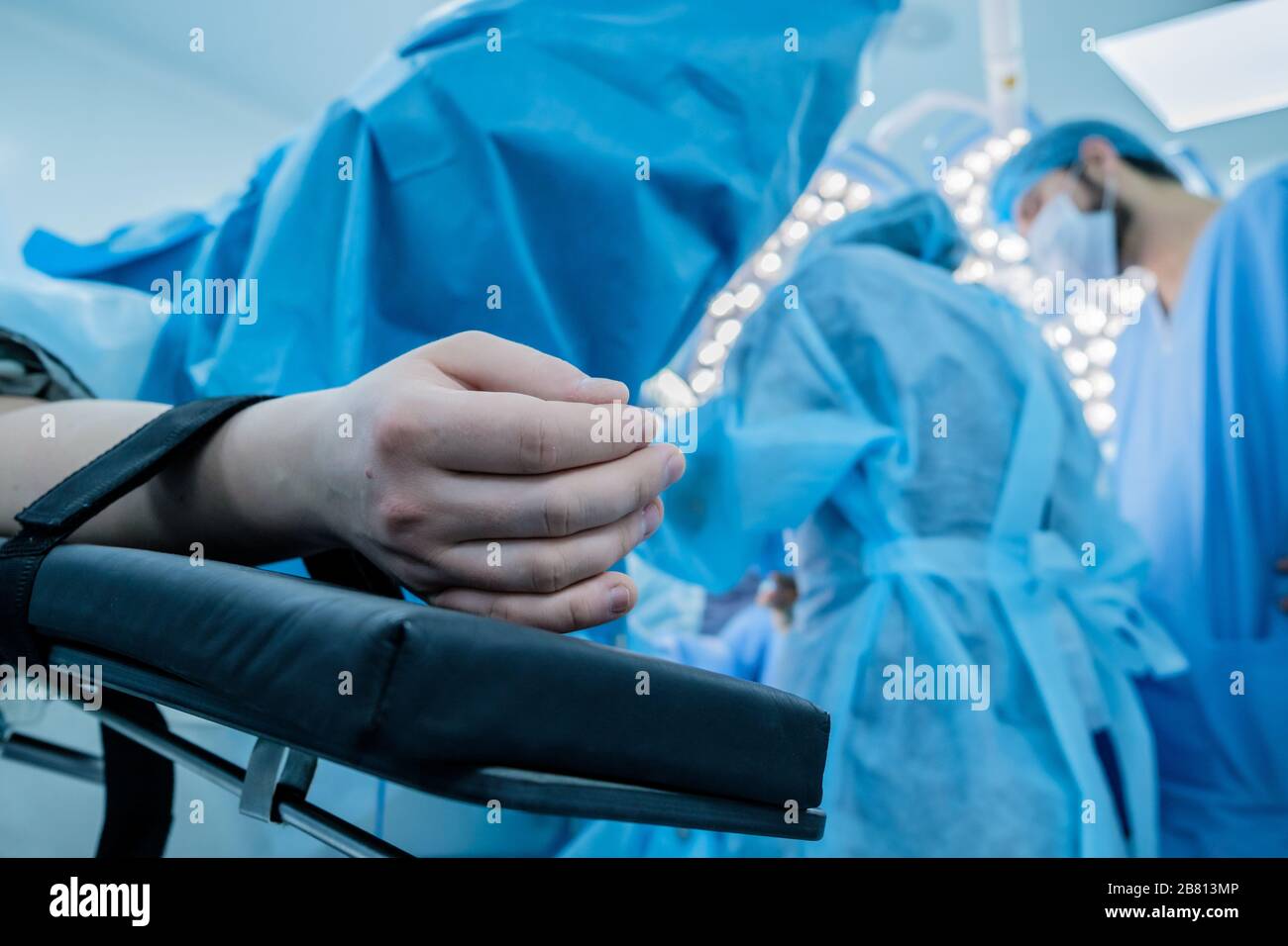 Mano di un paziente appoggiato sul tavolo operatorio. Il paziente dorme in anestesia generale. Sullo sfondo sono chirurghi in abiti chirurgici A. Foto Stock