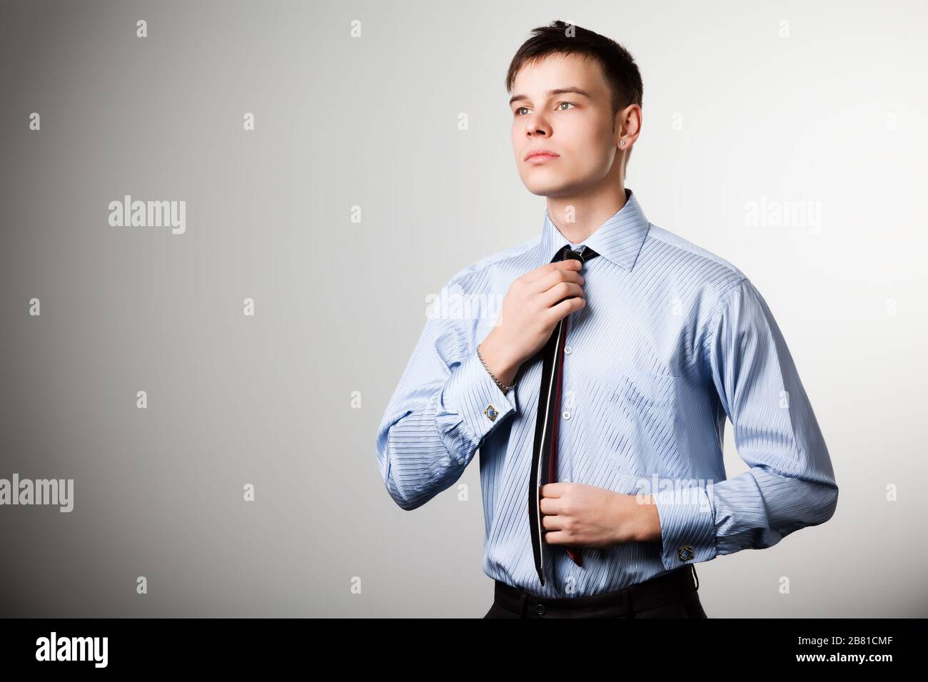 Uomo vestito con camicia blu e accessori orecchini e braccialetto argento,  raddrizza la cravatta nera Foto stock - Alamy
