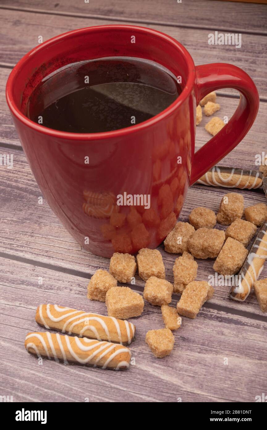 Tazza da tè in ceramica rossa, biscotti e pezzi di zucchero di canna su sfondo ligneo. Primo piano Foto Stock