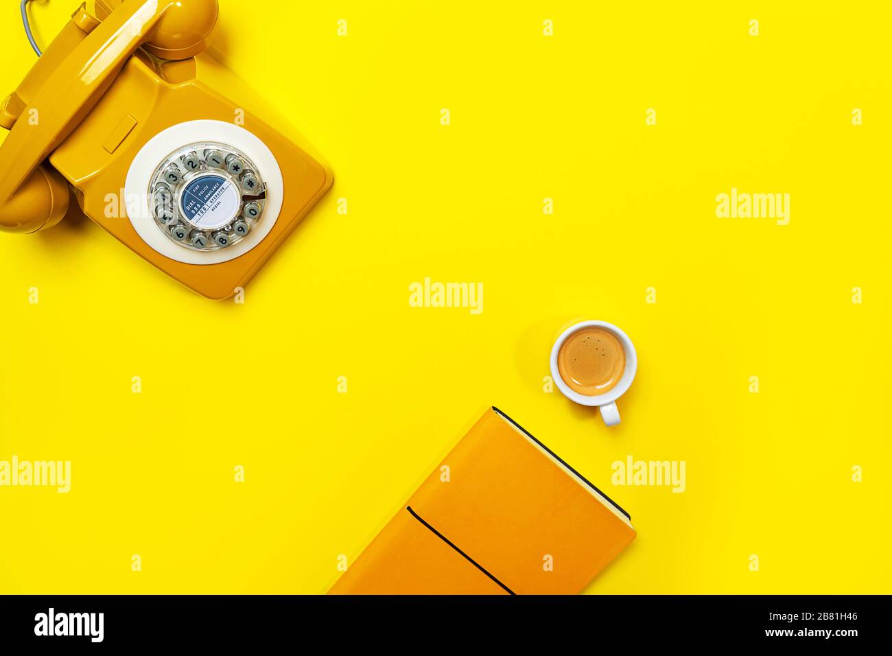 Disposizione gialla con telefono retrò rotante, tazza di caffè e notebook. Disposizione piatta, vista dall'alto, spazio copia. Foto Stock