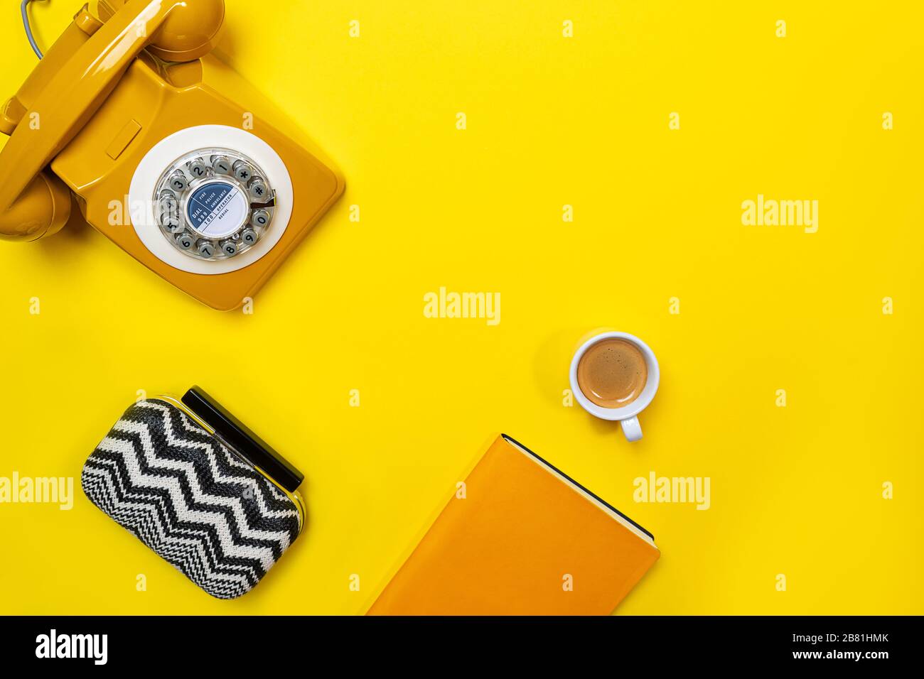 Disposizione gialla con telefono retrò rotante, tazza di caffè, borsa e notebook. Disposizione piatta, vista dall'alto, spazio copia. Foto Stock