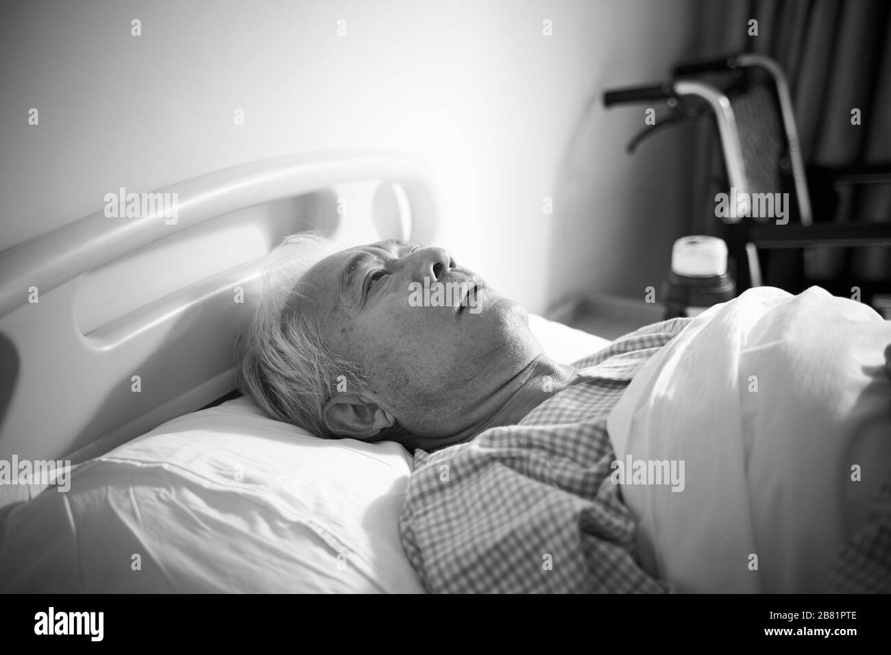 l'uomo asiatico anziano malato che giace nel letto dell'ospedale sembra essere triste e helpless, nero e bianco Foto Stock