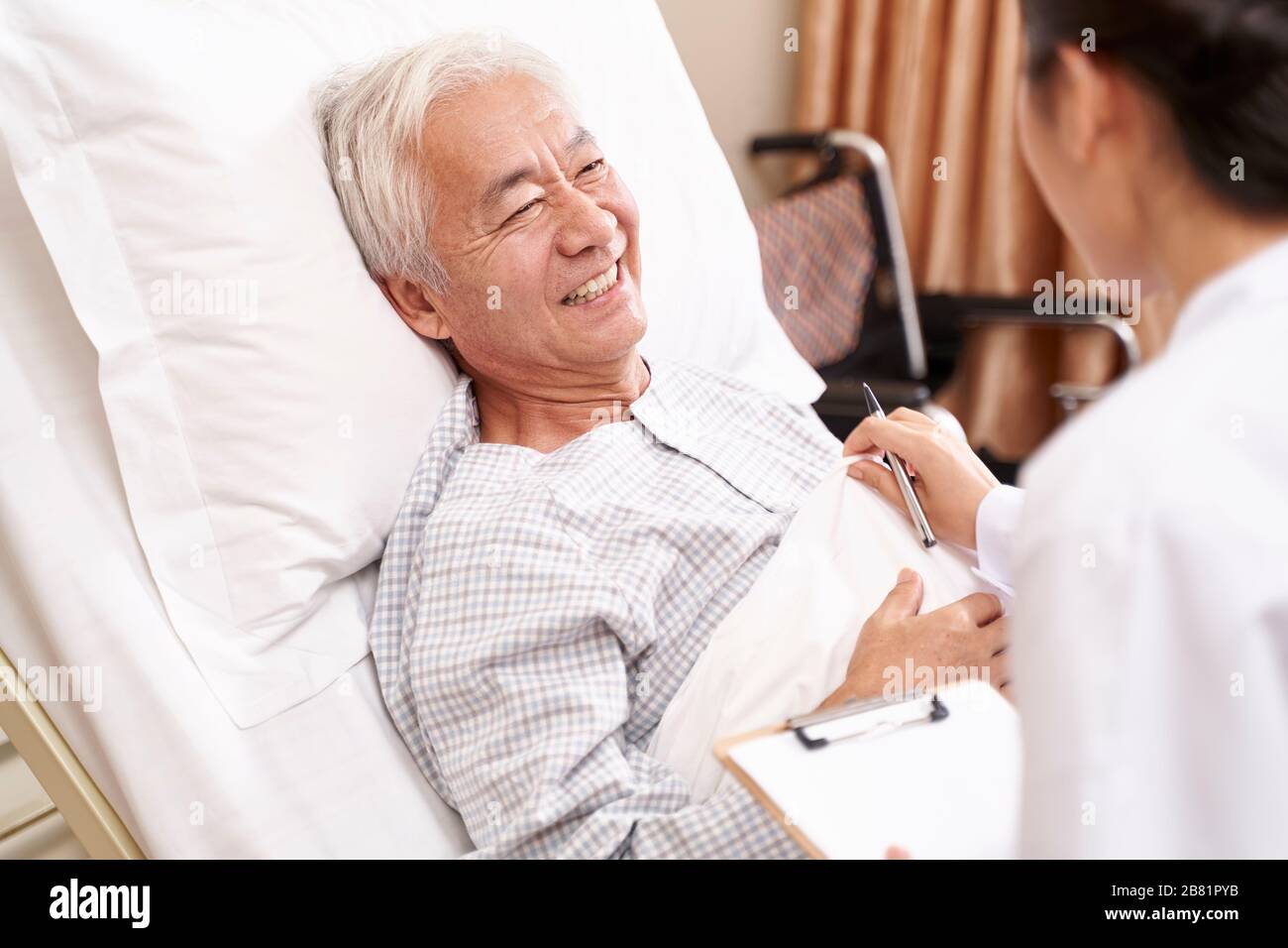 vecchio asiatico sdraiato a letto parlando con il giovane medico femminile in reparto ospedaliero Foto Stock