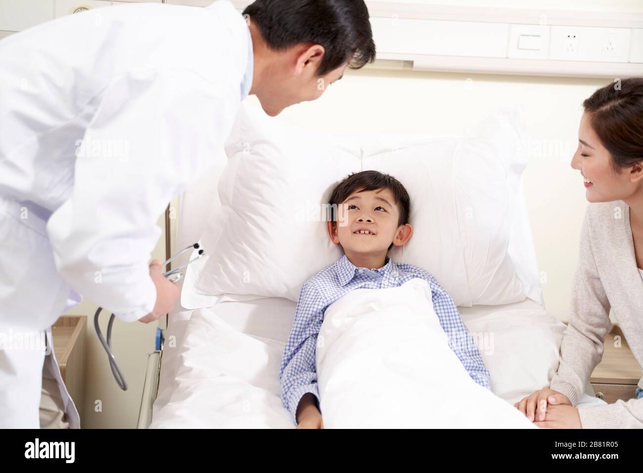 Cinque anni bambino asiatico che giace nel letto di ospedale accompagnato da madre a parlare con il medico Foto Stock