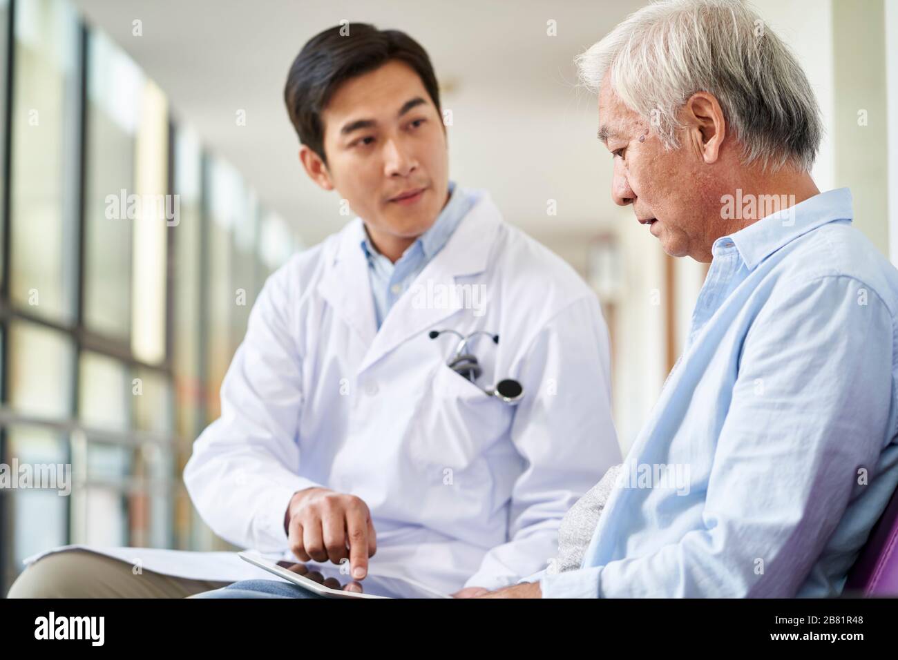 giovane medico asiatico che parla e spiega il risultato del test ai pazienti anziani in ospedale Foto Stock