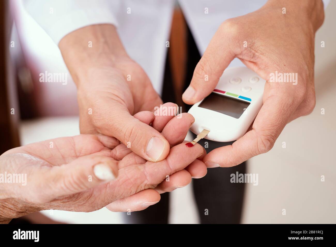 primo piano di un giovane uomo medico caucasico, indossando un cappotto bianco, circa per misurare il livello di glucosio nel sangue di una donna caucasica anziana in un glucometro Foto Stock