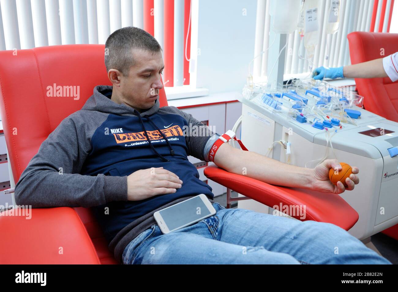 Giovane donatore seduto sul daybed e premendo la palla per una migliore pressione sanguigna Foto Stock
