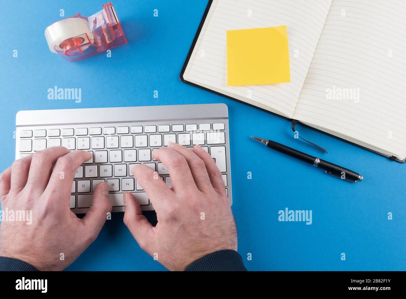 vista dall'alto della persona che digita sulla tastiera del computer sullo sfondo blu della scrivania con notebook aperto Foto Stock