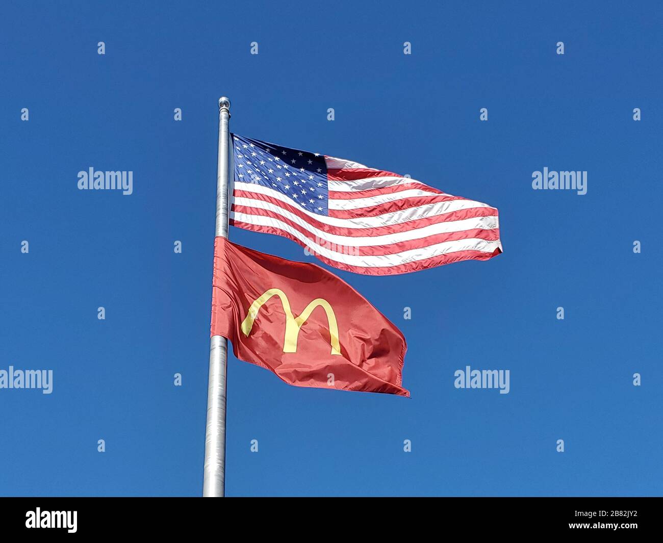 Primo piano del flagpole contro il cielo blu battenti bandiera americana e bandiera con il logo della McDonald's Corporation, Dublino, California, 23 febbraio 2020. () Foto Stock