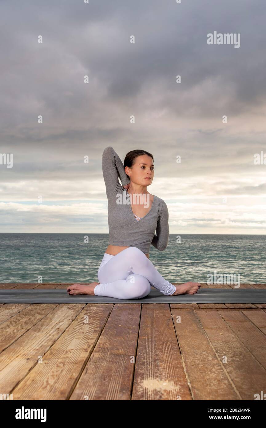 donna che pratica yoga sul mare, cielo drammatico Foto Stock
