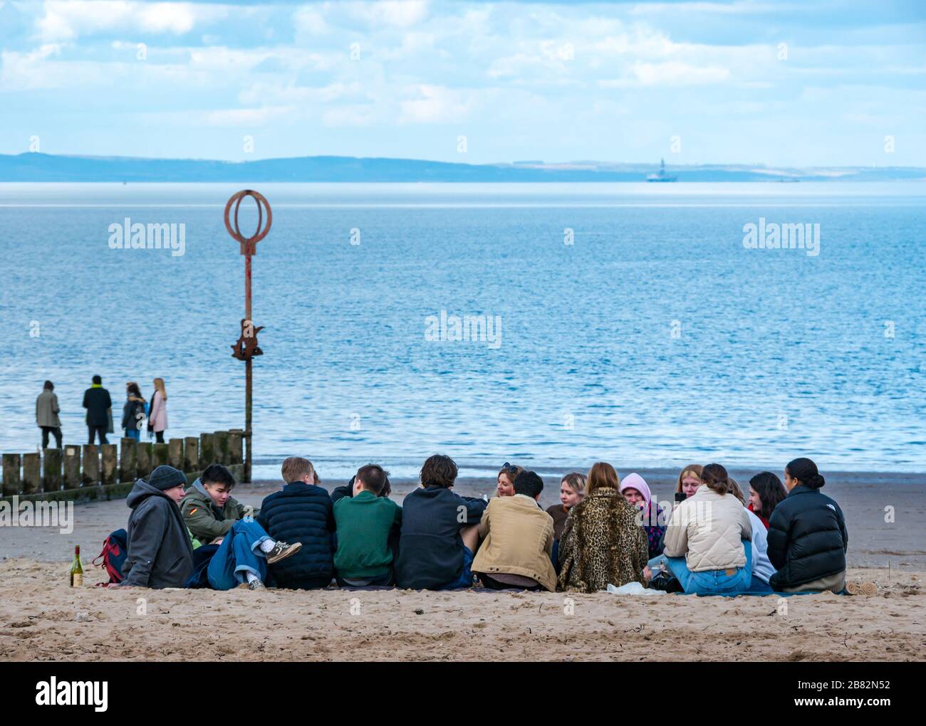 Portobello Beach, Edimburgo, Scozia, Regno Unito. 19 marzo 2020. In una soleggiata giornata primaverile, le persone si divertono al mare. Un gruppo di giovani si riuniscono per fare festa sulla spiaggia nonostante i consigli per mantenere la distanza sociale durante la pandemia di Coronavirus Covid-19 Foto Stock