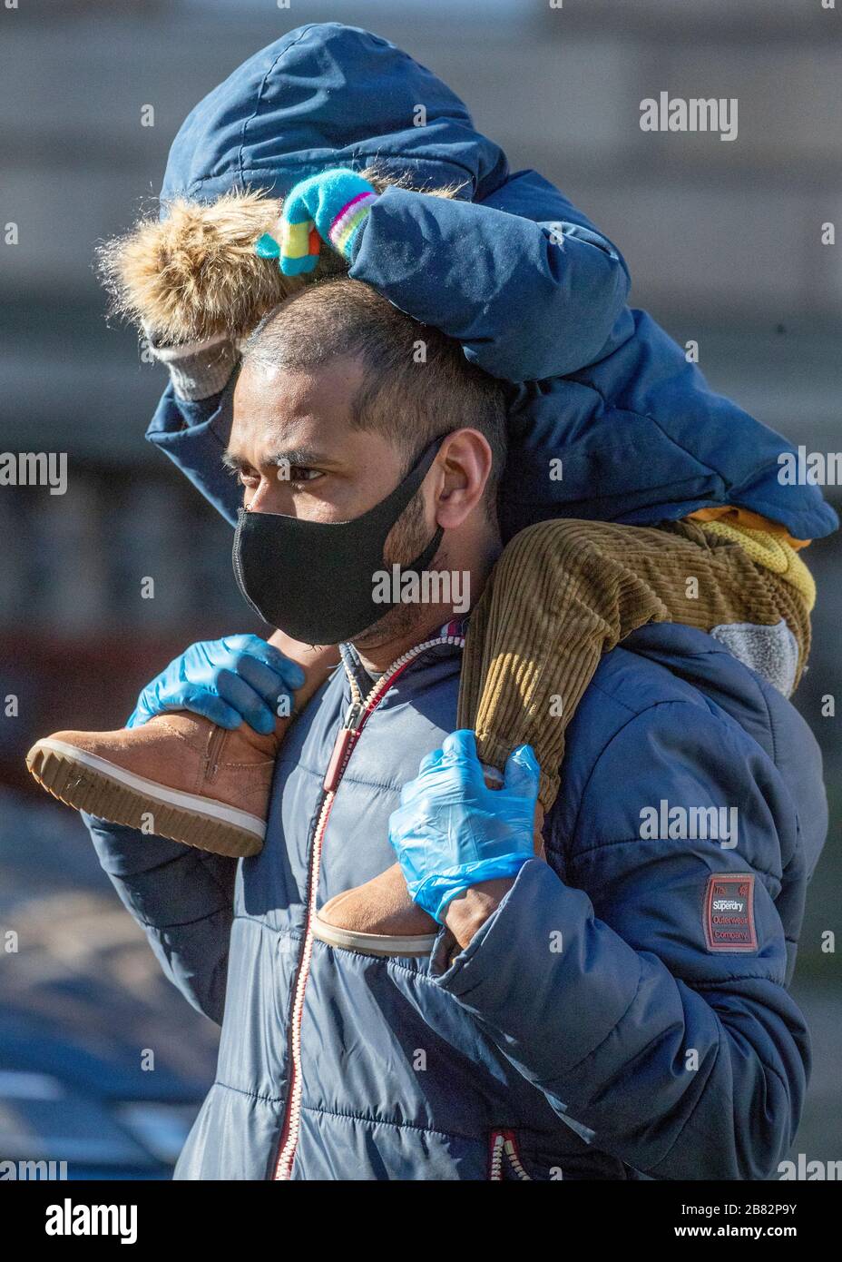 Un uomo indossa una maschera protettiva per il viso mentre porta un bambino sul Royal Mile di Edimburgo durante l'epidemia di coronavirus. Foto Stock
