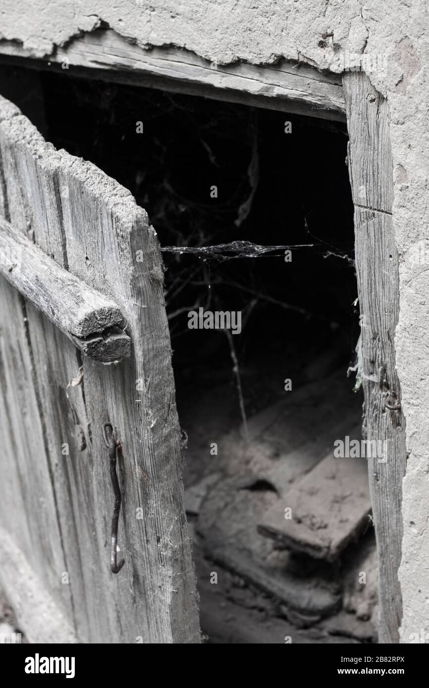 Una vecchia porta di legno intemperata leggermente aperta e ragnatela su uno sfondo scuro. Sfondo spaventoso Foto Stock