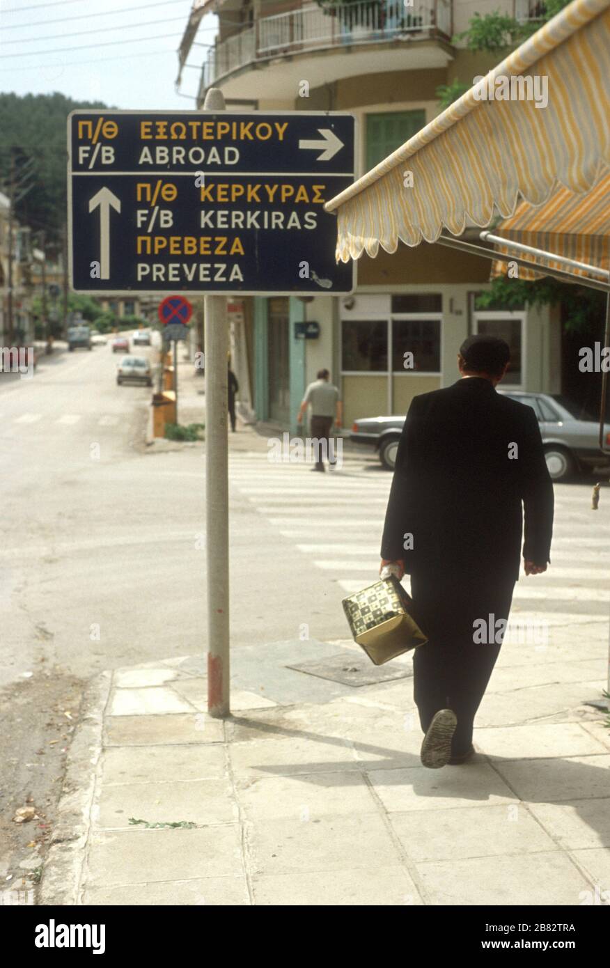 L'uomo greco porta i suoi acquisti sotto un cartello "all'estero" a Igoumenitsa, THESPROTIA, EPIRO, Grecia. Igoumenitsa è il principale porto di traghetti che serve la Grecia continentale nord-occidentale. I traghetti partono per le Isole IONIE e per l'Italia (o all'estero). Foto Stock