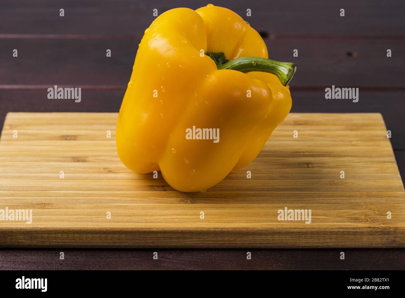Vista ravvicinata del pepe giallo con gocce d'acqua isolate su fondo di legno. Bellissimi sfondi natura. Foto Stock