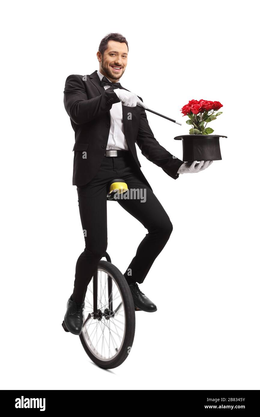 Ritratto a tutta lunghezza di un mago sorridente che nasconde un monociclo e che tiene la bacchetta e il cappello con i fiori isolati su sfondo bianco Foto Stock