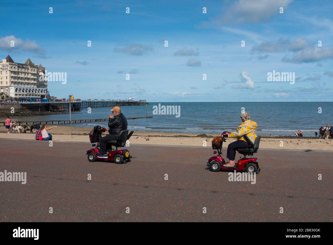 Uomo e donna su scooter per la mobilità sul lungomare di Llandudno, Galles, Regno Unito Foto Stock