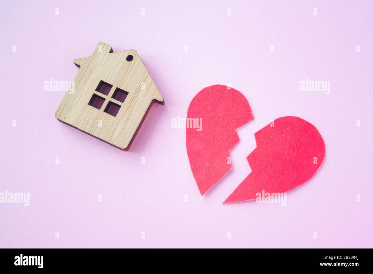 Divorzio, divisione della proprietà, povertà e nessun concetto di denaro. Casa di legno con cuore rotto su sfondo rosa brillante. Ipoteca, affitto, realtor Foto Stock