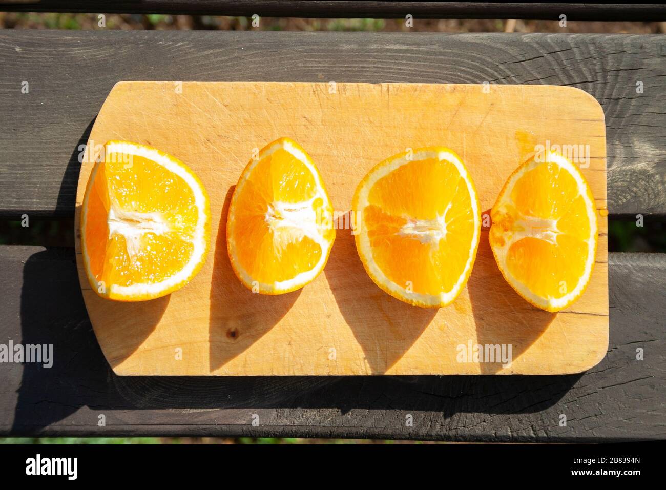 appetitosi pezzi tagliati di frutta arancione sul tagliere su un tavolo marrone in legno con luci solari. mangiare sano, frutta, vista dall'alto in estate Foto Stock