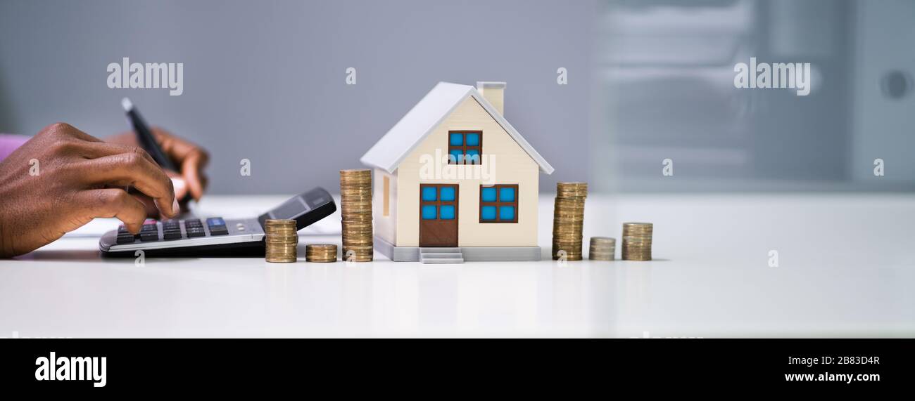 Imprenditore calcolo delle imposte dal modello di casa e delle monete metalliche in euro Foto Stock