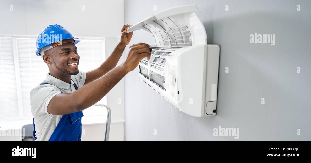 Felice giovane africano tecnico maschio riparare il condizionatore d'aria Foto Stock