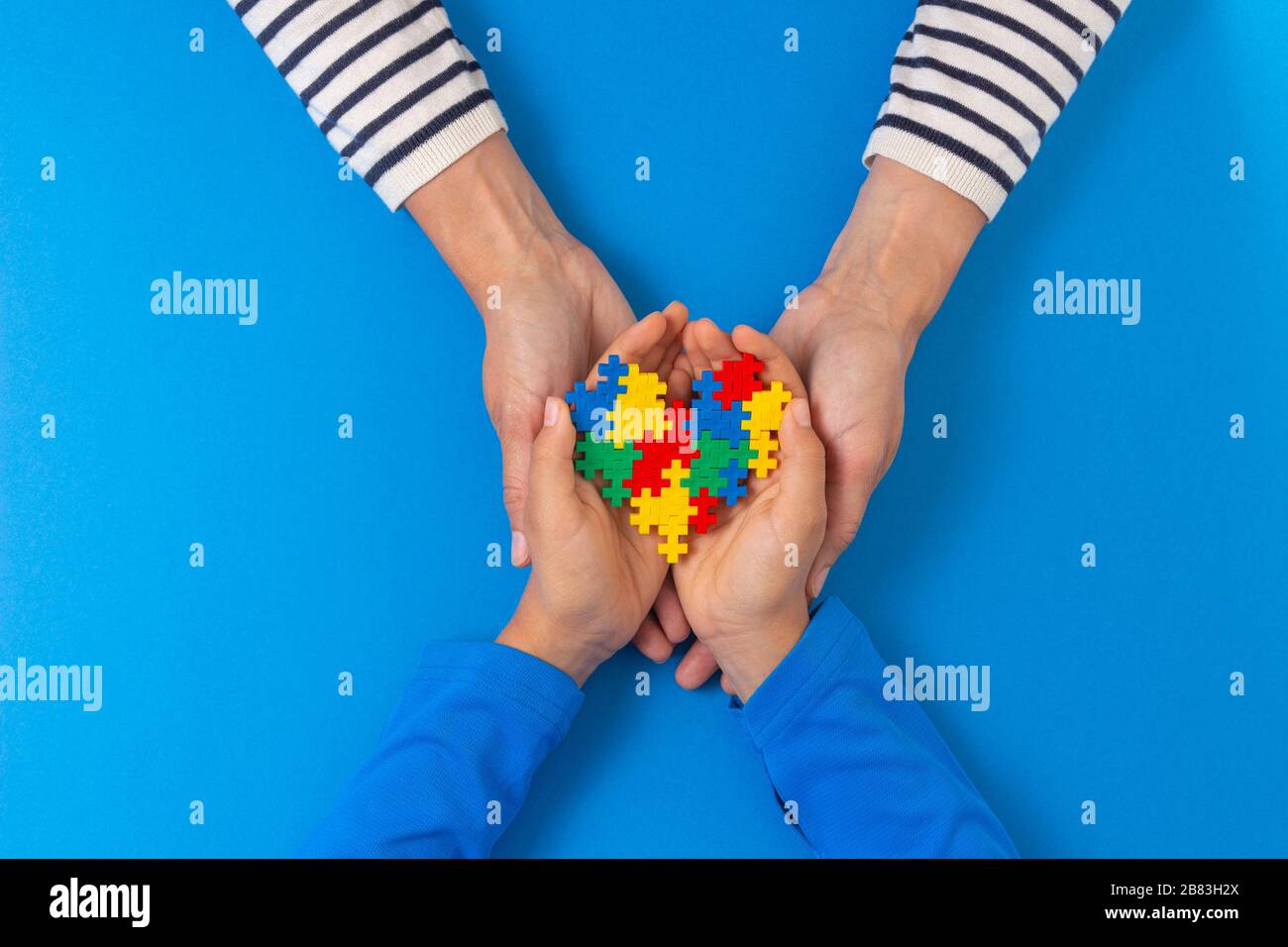 Concetto del giorno di consapevolezza di autismo del mondo. Le mani di bambino e femmina tengono il cuore del puzzle su sfondo blu chiaro Foto Stock