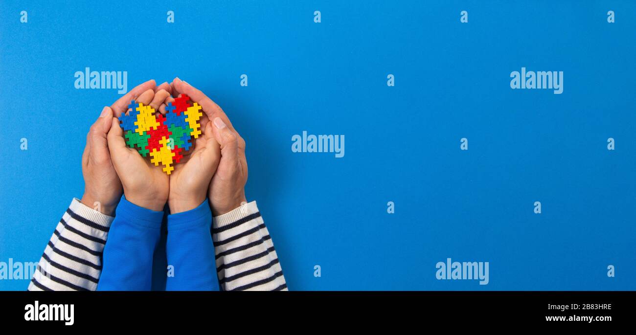 Concetto del giorno di consapevolezza di autismo del mondo. Mani per adulti e bambini che tengono il cuore del puzzle su sfondo blu chiaro Foto Stock