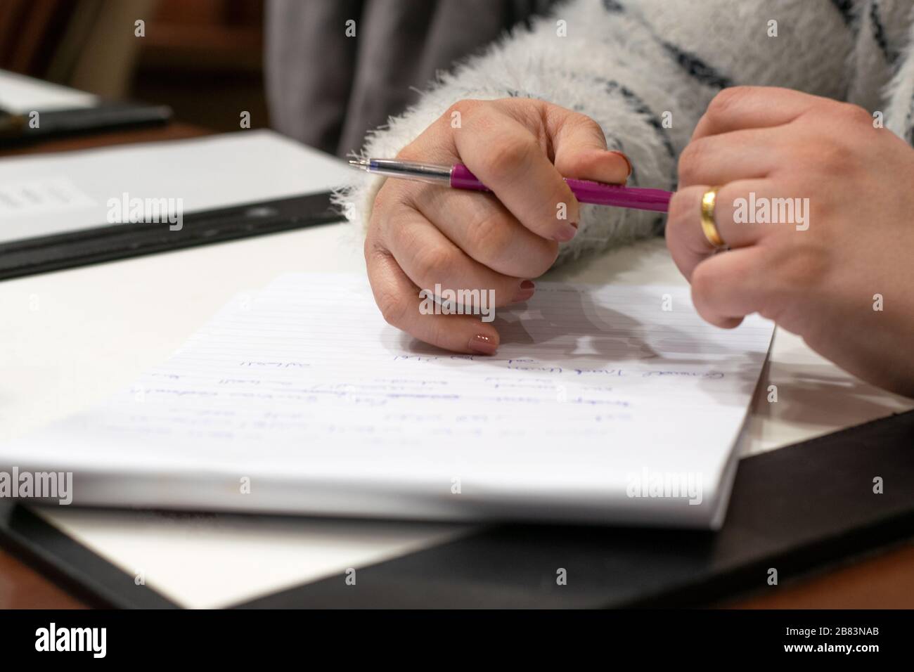 Primo piano sulle mani di una donna tenendo una penna sopra una nota. Foto scattata a Beirut, Libano Block su un tavolo da riunione in una sala conferenze Foto Stock