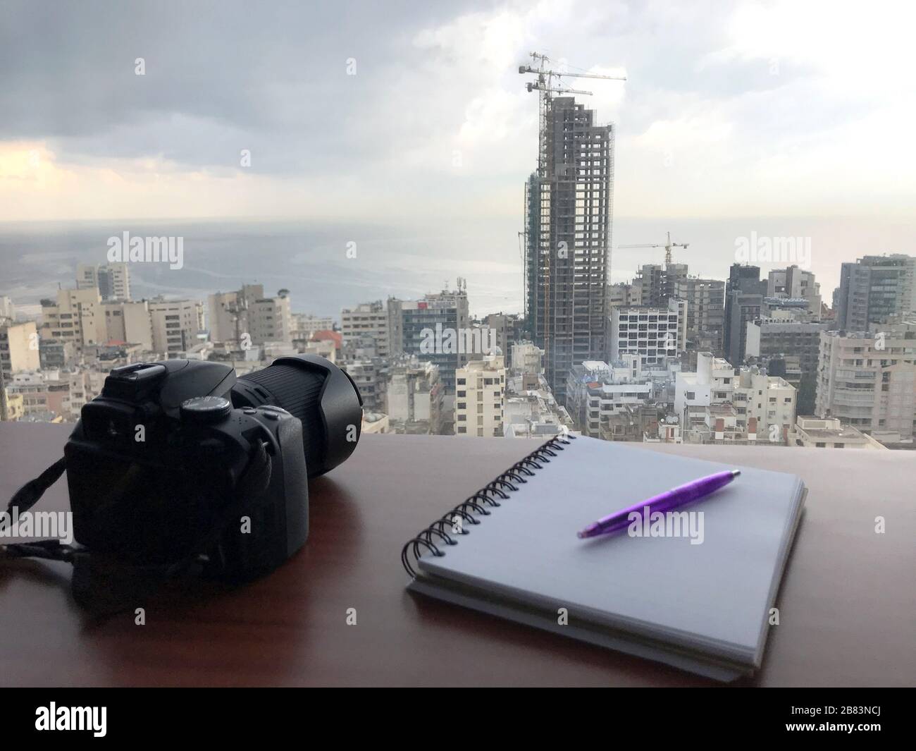Macchina fotografica, penna e blocco note in primo piano con una bella, un po 'astratta, vista della città, al mattino. Foto scattata a Beirut, Libano Foto Stock