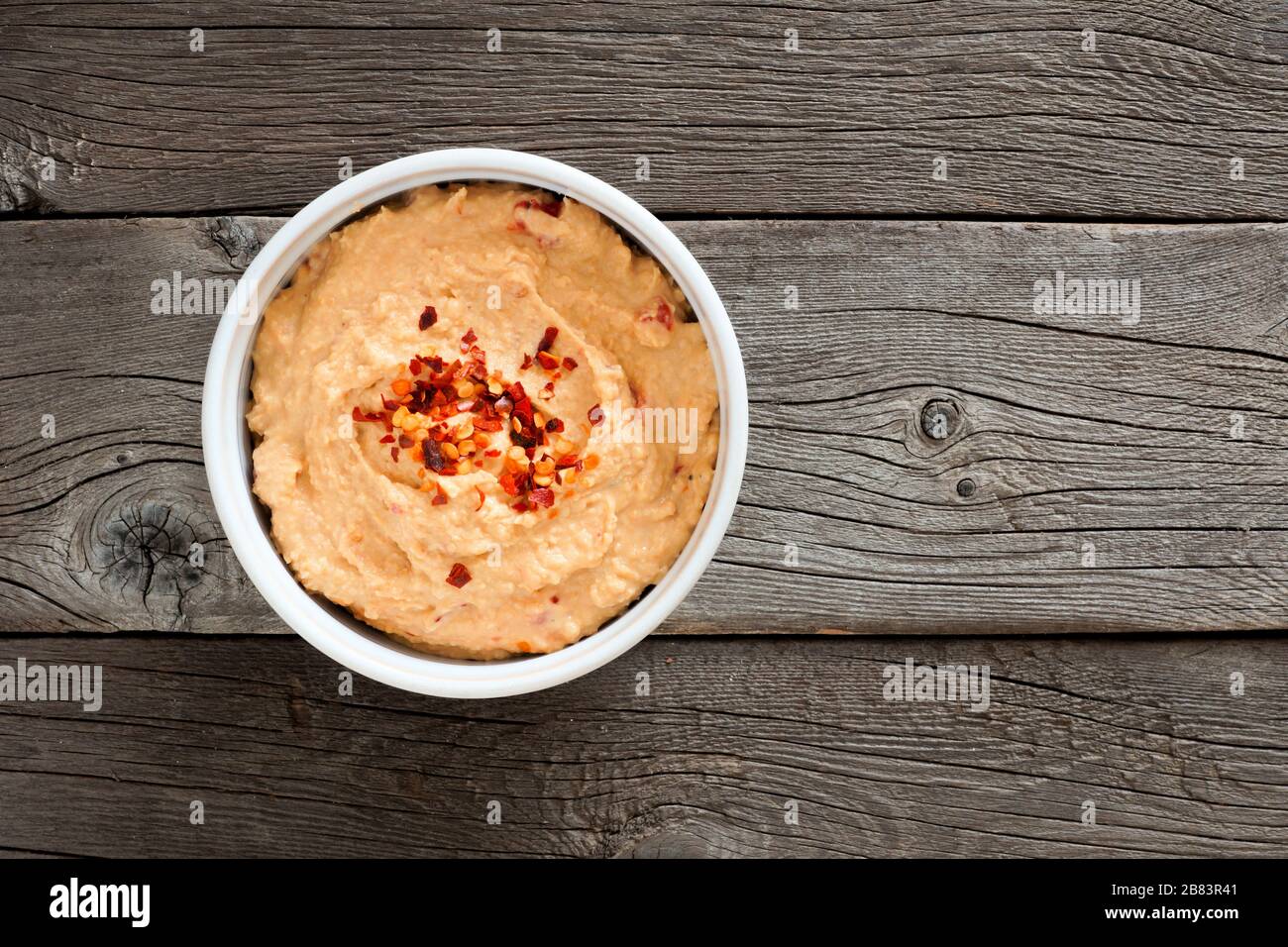 Ciotola di hummus piccante, vista sopra un rustico sfondo di legno Foto Stock